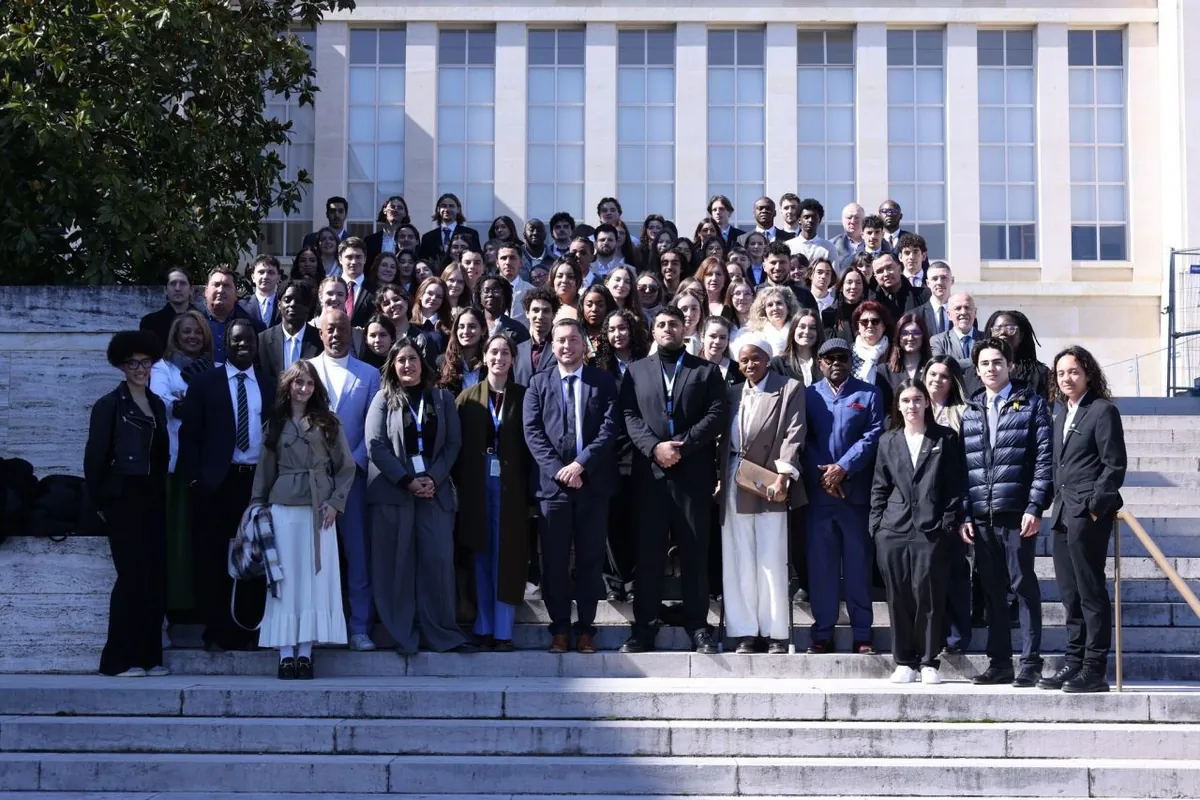A large group gathered on the steps of the Palais des Nations in Geneva, in front of the tall-windowed façade.