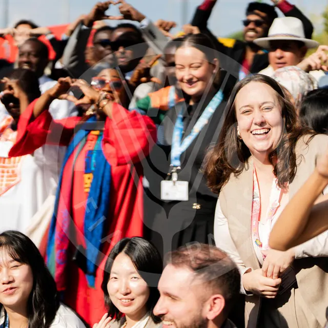 Young World Food Forum participants gathered outdoors, smiling; several make heart shapes with their hands.