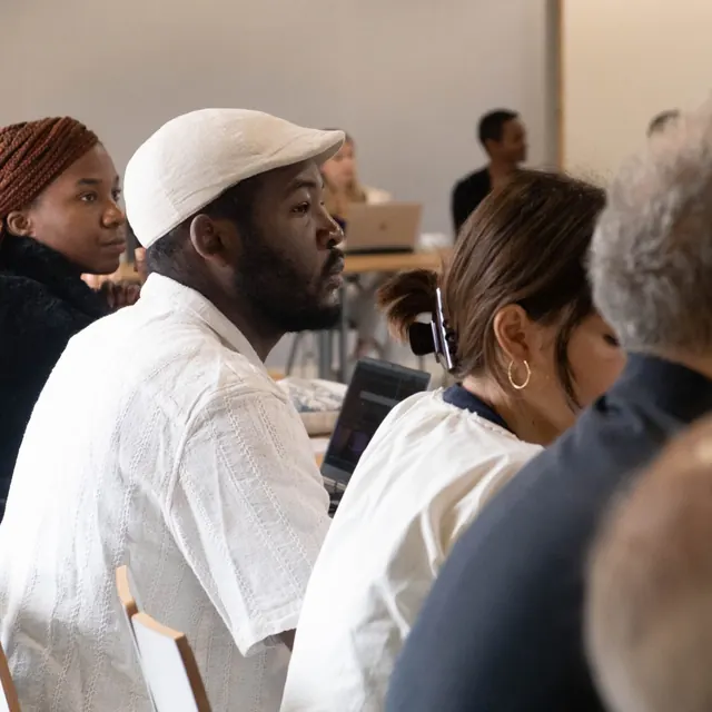 Participants listening closely during a workshop, seated at tables with laptops.